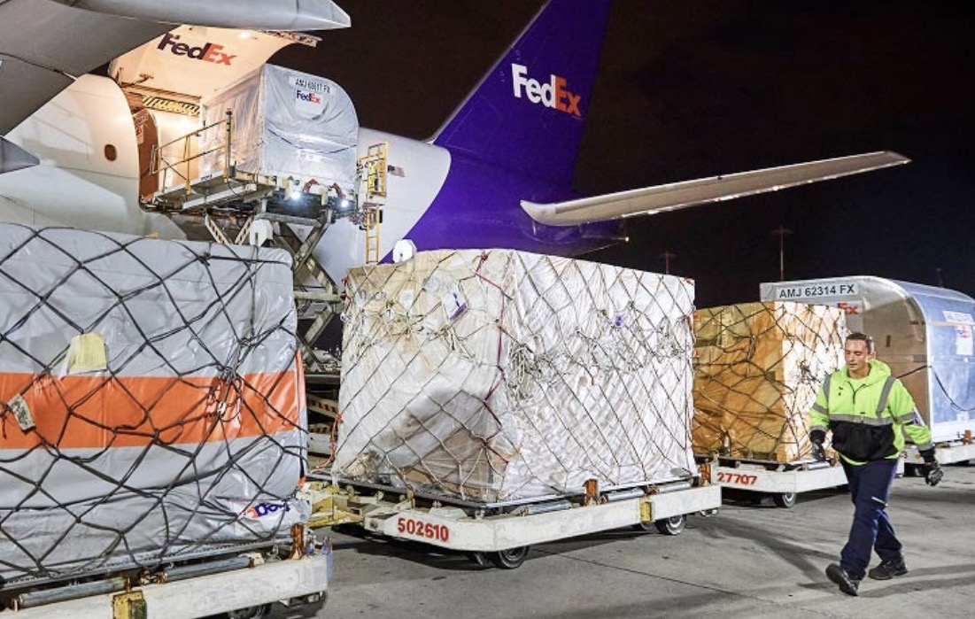 Ground crew loading netted cargo containers onto a FedEx Boeing 777F at night